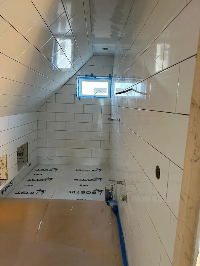 Väggar och snedtak färdigkaklade i blankvitt kakel, fönstret skyddat med tejp.